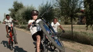 Foto van drie jongetjes op fietsen die op straat aan het stuntfietsen zijn.