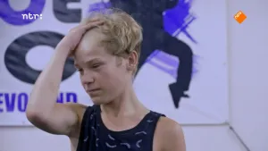 Foto van jongen, danser, je ziet vooral zijn hoofd, met op de achtergrond muur met afbeeldingen erop.