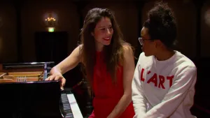 Foto twee vrouwen die samen achter een piano, vleugel, zitten.
