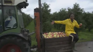 Foto van presentator die buiten in fruitgaard zit naast een grote kist helemaal vol met appels.