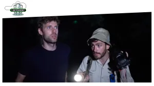 Foto van twee mannen die buiten in het donker lopen, één van hen houdt een brandende zaklamp vast.