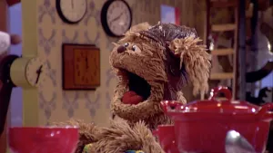 Foto van scène uit Sesamstraat met Tommie die zit aan tafel met rode pan, beker en bak erop in de studio.