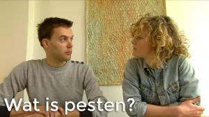 Foto van scène uit Sesamstraat met man en vrouw die zitten in de studio, erbij de tekst "wat is pesten?".