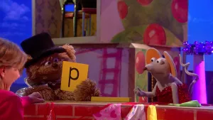 Foto van scène uit Sesamstraat met Tommie met hoge hoed op die de letter P vasthoudt, erbij zit ook Ieniemienie.