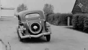 Oude foto, zwart/wit, van een auto op straat.