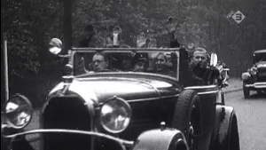 Oude foto, zwart/wit, van een auto met NSB'ers erin die rijdt op straat.