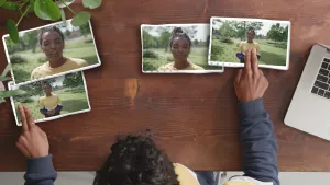 Foto van persoon van bovenaf gezien die aan tafel zit waarop aantal foto's, portretten, van een vrouw liggen en die diegene rangschikt.