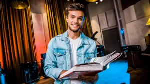 Foto van presentator in de studio die een groot boek vasthoudt.