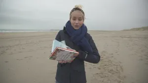 Foto van presentator die staat op het strand en een paar kinderboeken in haar handen vast heeft.