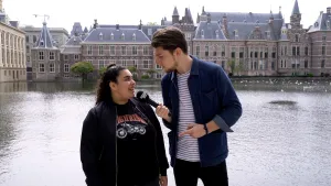 Foto van presentator die meisje interviewt met microfoon in de hand, op de achtergrond het Binnenhof te Den Haag.
