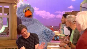 Foto van scene uit Sesamstraat met Pino en op de voorgrond verschillende mensen, in de studio.