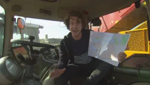 Foto van man in tractor/landbouwmachine die een grote kaart van de omgeving vasthoudt.
