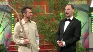 Foto van de studio van Snugger met de presentator en bij hem staat een man die een lange stok vasthoudt.