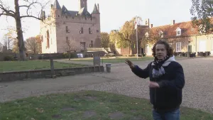 Foto van presentator die staat in kasteel tuin met ook Kasteel Doornenburg in beeld, hij wijst naar dat kasteel.