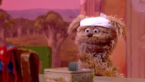 Foto van Sesamstraat waarbij Tommie aan tafel zit in de studio met een roze feestmutsje op, voor hem staat een koekjestrommel.