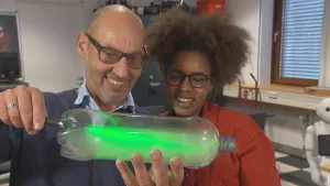 Foto van man en vrouw die in een laboratorium een doorzichtige fles vasthouden met daarin groen lichtgevende vloeistof.
