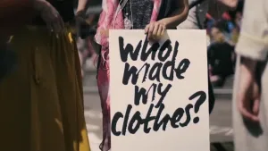 Foto van mensen op straat, één ervan houdt bord vast met de tekst "who made my clothes?".
