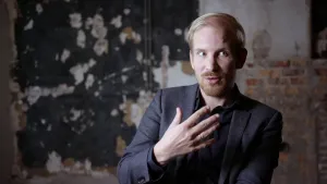 Foto van presentator in een lege kamer met stenen muren.