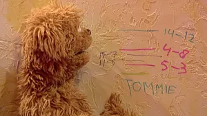 Foto van een figuur uit Sesamstraat, Tommie, die staat bij een muur waarop lijntjes staan die de grootte aanduiden van personen.