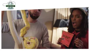 Vrouw en man die in kamer staan, de man houdt een grote lange geelbruine slang vast.