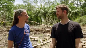 Foto van een kale plek in een regenwoud waarvoor twee mannen staan die met elkaar in gesprek zijn.
