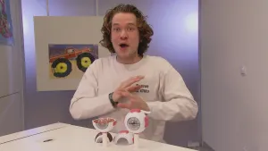 Foto van presentator die aan tafel zit waarop twee modelletjes van het oog staan.
