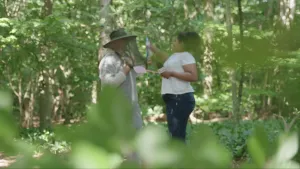 Foto van man met hoed op en een vrouw met vliegenmepper die staan in een dicht groen bos.