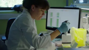 Foto van vrouw, laborante, aan bureau met computer die een DNA-proef/onderzoek uitvoert.