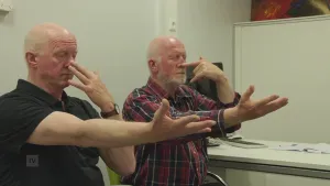 Foto van twee mannen in een behandelkamer die bepaalde oefeningen doen met hun handen en armen.