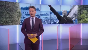 Foto van presentator in studio met foto op de achtergrond waarbij je de NSB'er Mussert ziet met publiek.