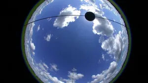 Bolvormige foto van een blauwe lucht met witte en grijze wolken, eroverheen zwarte lijn met ergens een zwart bolletjen.