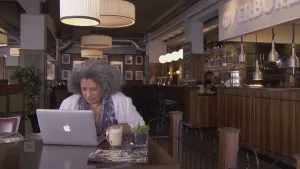 Foto van vrouw die in café aan tafel zit achter een laptop.