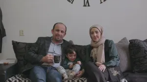 Foto van gezin, vader, moeder, klein kind, uit Syrië die op grote bank in huiskamer zitten.