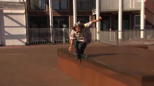 Foto van een skater die gaat over een laag muurtje buiten bij een gebouw.