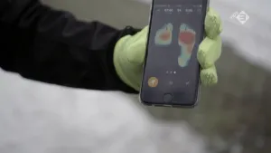 Hand met handschoen aan die een smartphone vasthoudt met erop afbeelding van twee voetafdrukken.