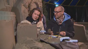 Foto van twee mannen die binnen bezig zijn met een hoop zand, ze maken een zandsculptuur.