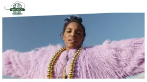 Foto van vrouw met lilaroze kledij aan en een goudkleurige ketting om, je ziet haar hoofd en armen.