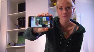 Foto van presentator in kamer die een smartphone vasthoudt waarop een foto te zien is op het beeldschermpje.