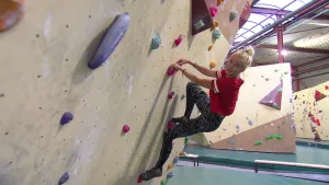Foto van een boulderbaan, indoor, in grote zaal, met een vrouw die erin klimt.