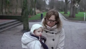 Foto van een moeder met kind die ze draagt in een park.