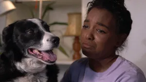 Foto van huilend meisje bij een vrolijk kijkende hond, je ziet alleen het hoofd en de kop van de hond.