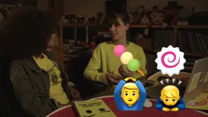Foto van twee vrouwen aan tafel met ervoor vier emoticons afgebeeld.