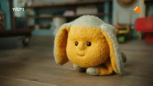 Foto van Dropje (pop) die zit op de vloer in een kamer.
