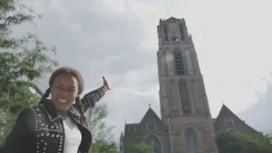 Foto van vrouw, vrolijk lachend, die wijst naar een hoge kerktoren.