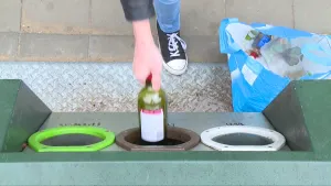 Foto van deel van een glasbak, je ziet nog hand van een persoon die een fles in één van de openingen ervan gooit.