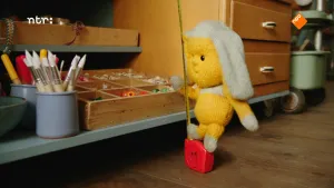 Foto van Dropje, een stoffen pop, die staat op een rolmaat bij een kast met speelgoed.