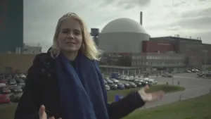 Foto van presentator die buiten staat voor een kerncentrale.