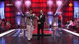 Foto van de studio van Snugger met de presentator die op het podium staat samen met een andere man, op de achtergrond deel van het publiek.