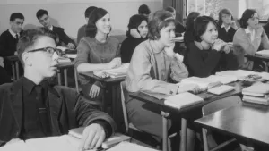 Oude foto, zwart/wit, van leerlingen, jongens en meisjes, in klaslokaal van middelbare school.