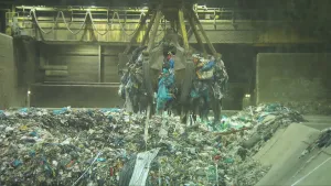 Foto van fabriekshal met op de grond afval waarbij een grijper deel ervan oppakt.